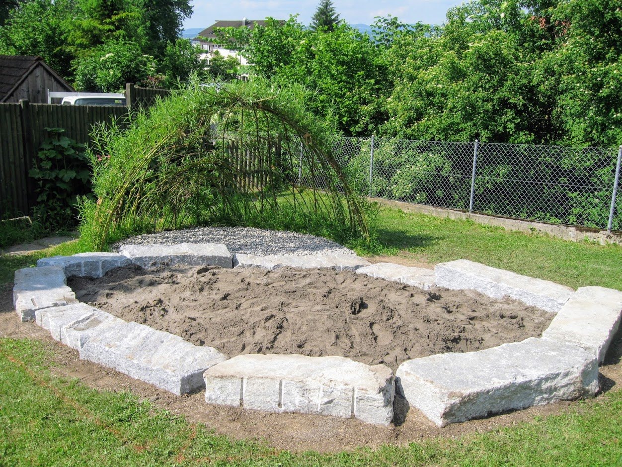 Sandkasten mit Natursteinquadern und Weidenbogen